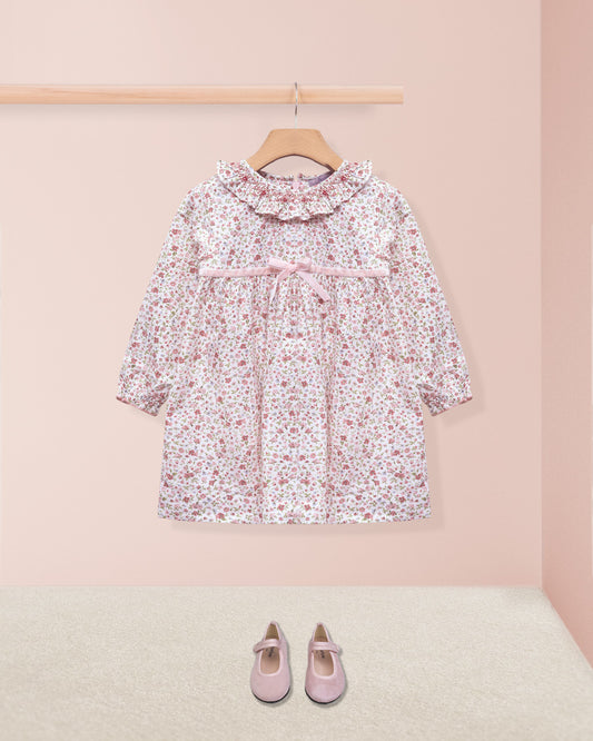 Floral dress on a hanger with pink shoes on the floor against a pink wall