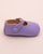 Side view of a lavender leather baby crib shoe with scalloped edge and velcro strap, shown against a pale pink backdrop.