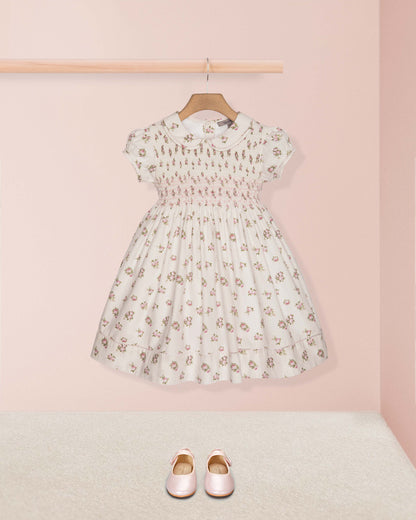 Floral dress on a hanger with pink shoes on the floor against a light pink wall.