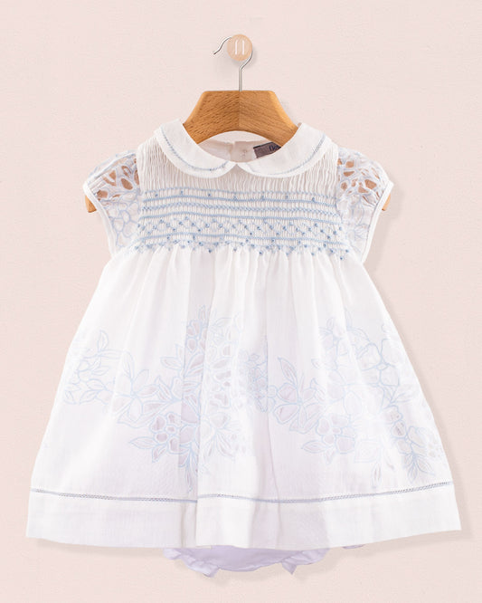 Front view of Baby Emmy Doppia Blue Smock Dress Set hanging on a wooden hanger showing blue hand smocking and floral embroidery on white cotton fabric