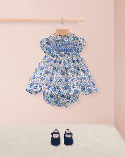 Baby Emmy Liberty Blue Rosebud Mini Dress Set with smocked bodice, entre-deux stitching, matching bloomers, and navy Mary Jane shoes on a pink backdrop.