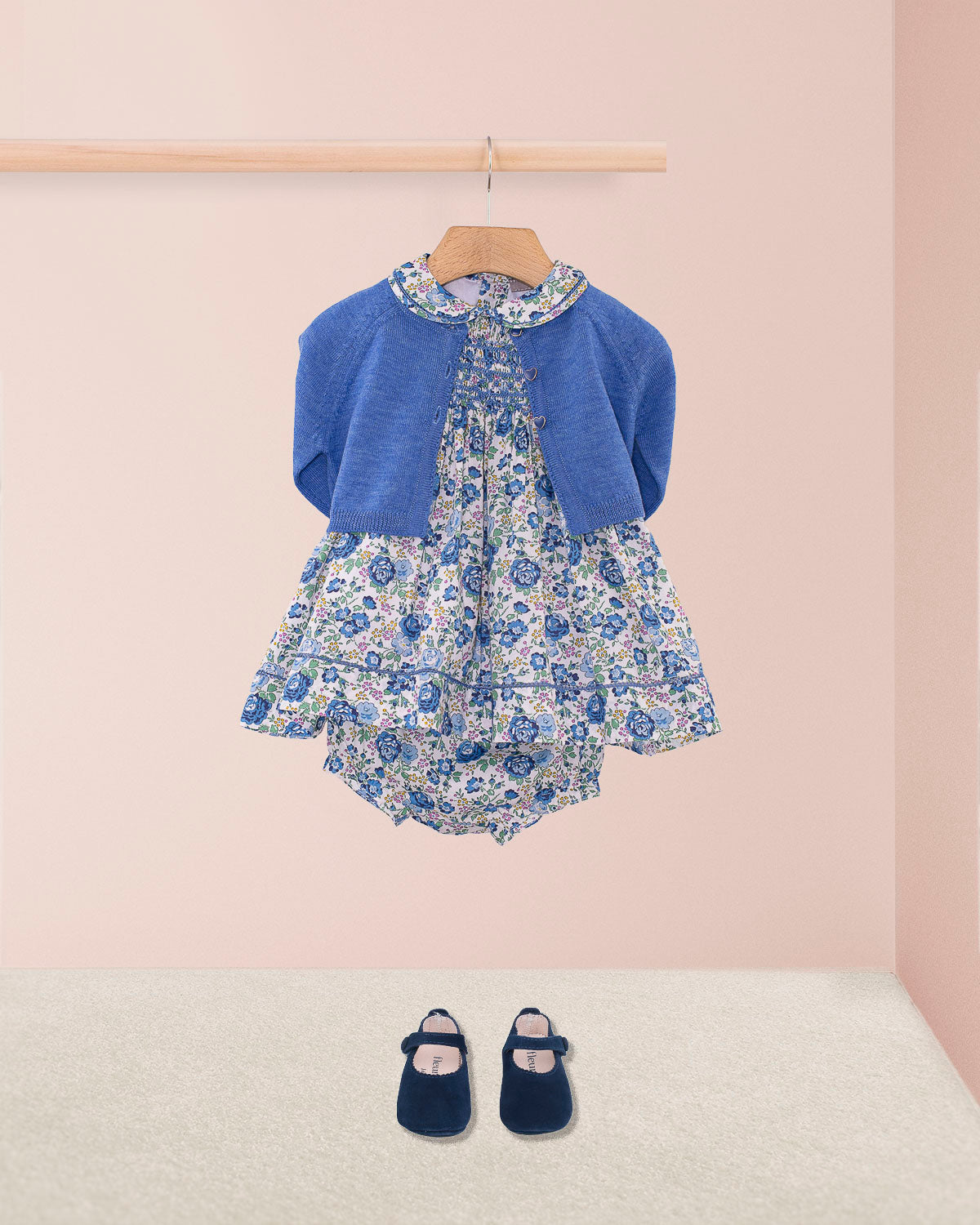 Baby Emmy Liberty Blue Rosebud Mini Dress Set, featuring a floral dress with smocked bodice and entre-deux stitching, paired with bloomers and a cerulean knitted cardigan.