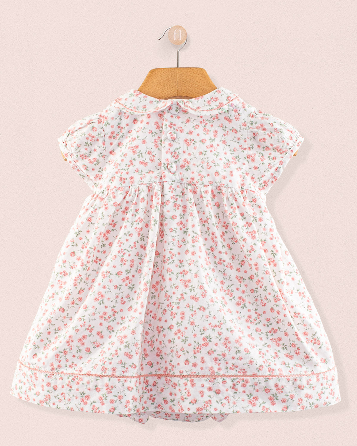 Back view of the Baby Emmy Elegant Pink Floral Dress showing centered button closure, Peter Pan collar, floral print throughout, and gathered skirt. Dress is displayed against a soft pink background.