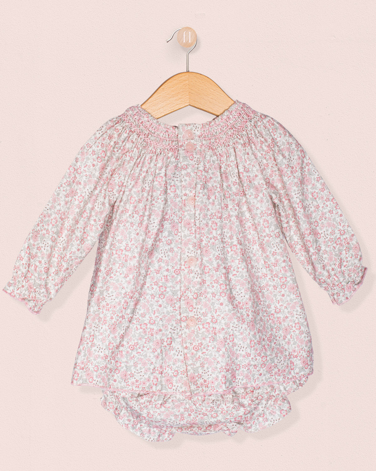 Floral baby romper on a hanger against a light pink background