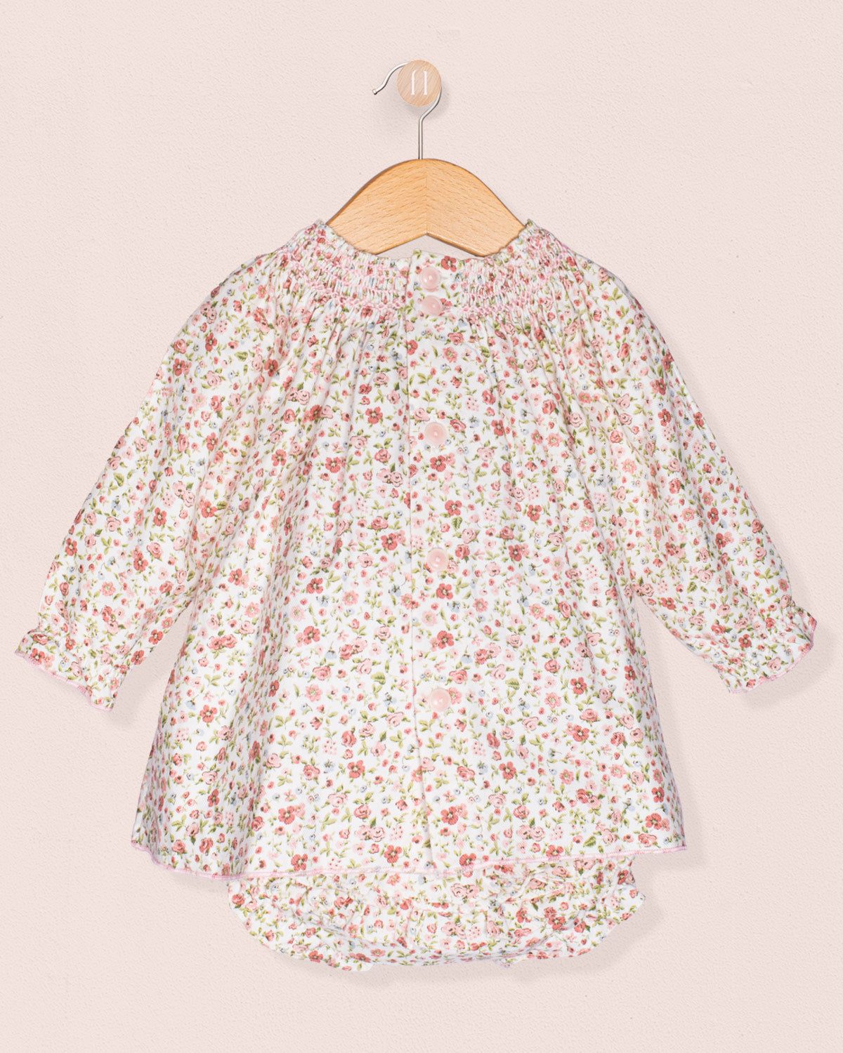 Floral dress on a wooden hanger against a light pink background