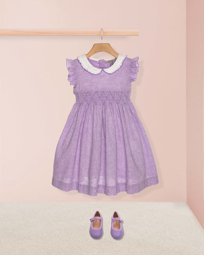 Purple dress with white collar on a hanger against a pink wall.
