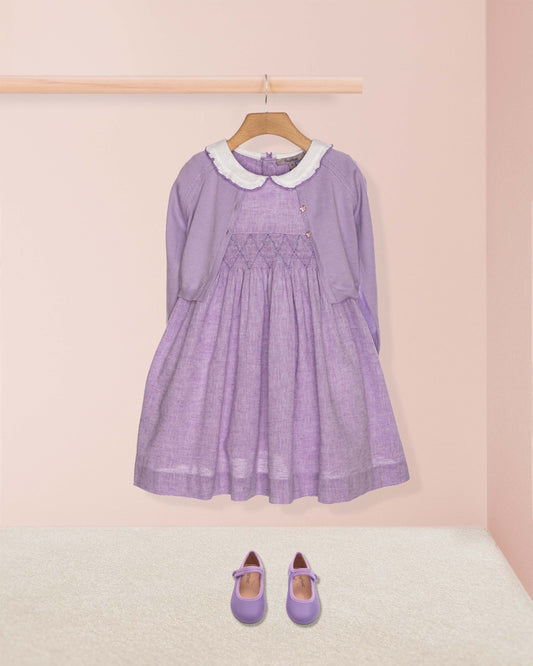 Purple dress with white collar on a hanger against a pink wall.