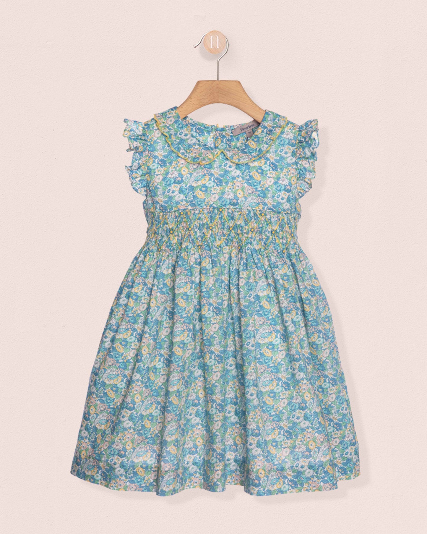Blue floral dress on a hanger against a light pink background