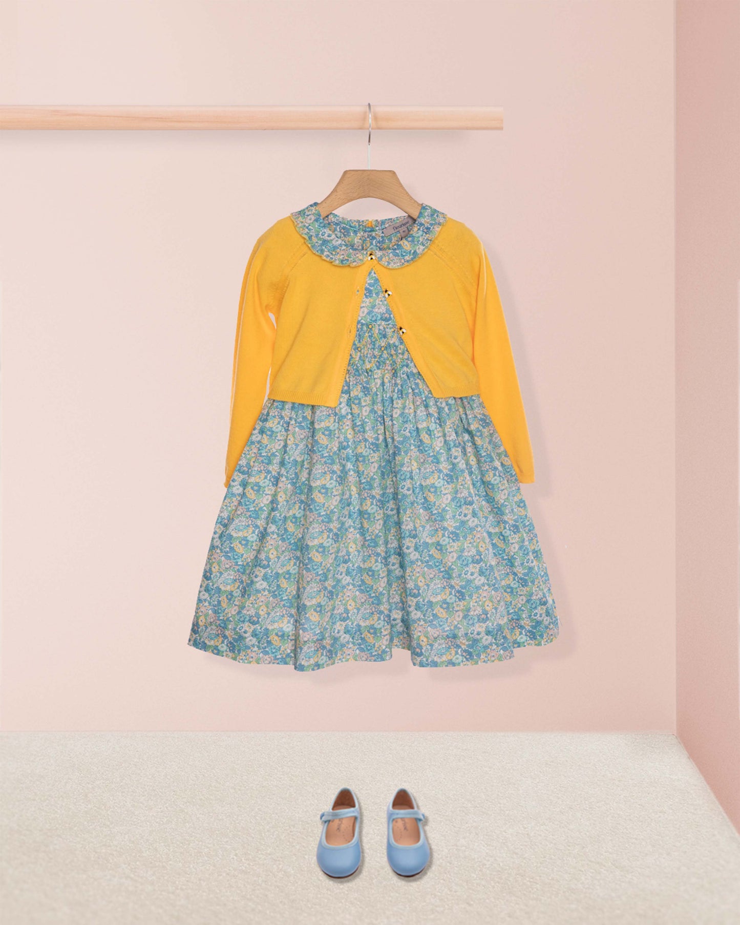 Floral dress with yellow cardigan and blue shoes on a pink background