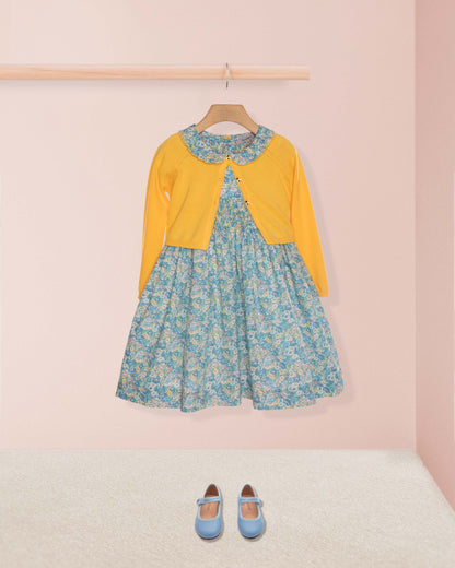 Floral dress with yellow cardigan and blue shoes on a pink background