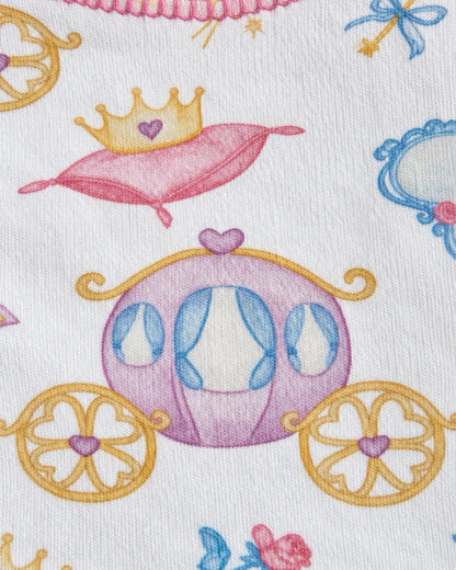 A close-up of a white fabric printed with a whimsical fairy tale pattern featuring a pink and purple carriage, a pink pillow with a gold crown, and blue and pink floral details.