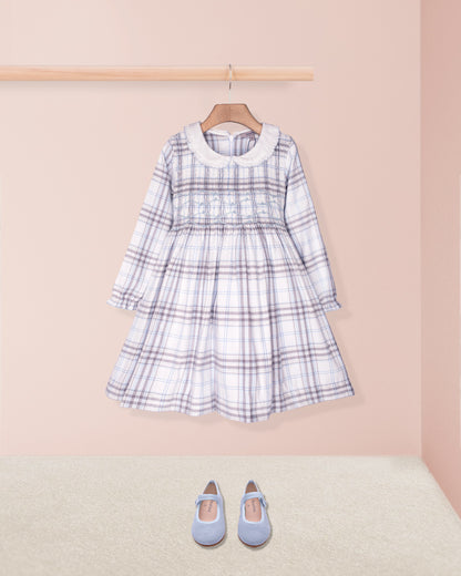 Plaid dress with long sleeves and a collar on a hanger, accompanied by blue shoes on a beige floor.