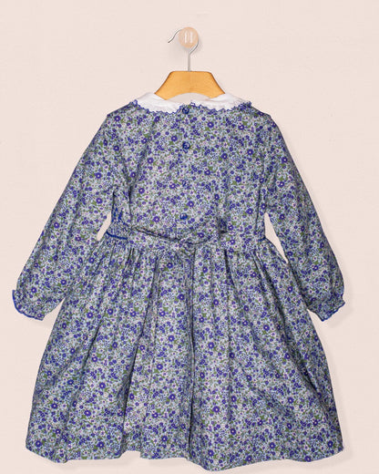 Back view of the Fiorella dress hanging on a wooden hanger, highlighting the tie-back sash and gathered waist against a soft beige background.