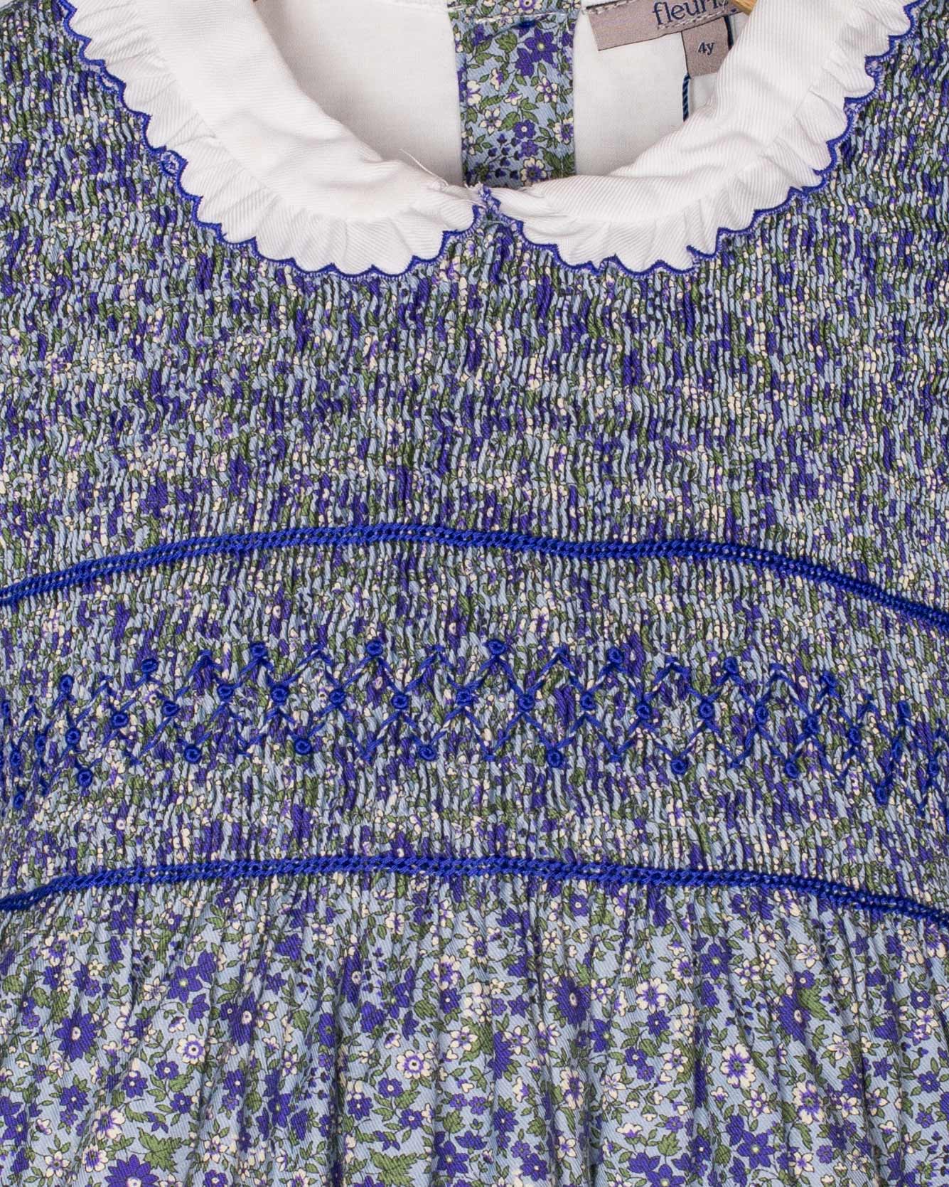 Detailed close-up of the smocked bodice on the Fiorella Mini Blue Floral Twill Dress, showing the fine hand-smocking, floral pattern, and ruffled white collar.