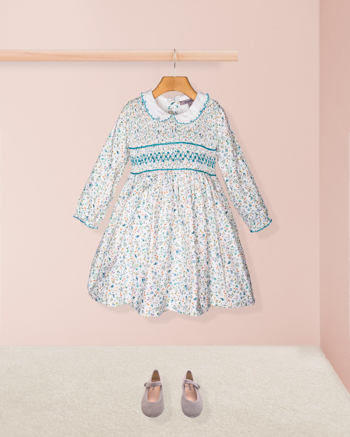 Floral dress with long sleeves on a hanger against a pink wall.