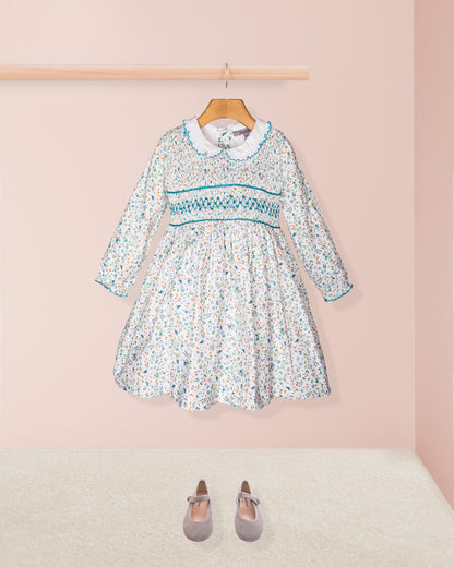 Floral dress with long sleeves on a hanger against a pink wall.