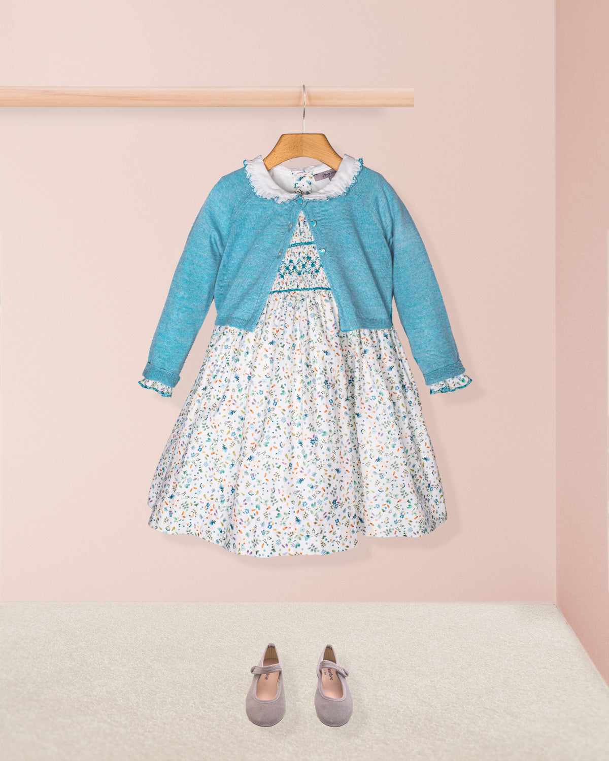 Children's outfit with floral dress and blue cardigan on a pink background