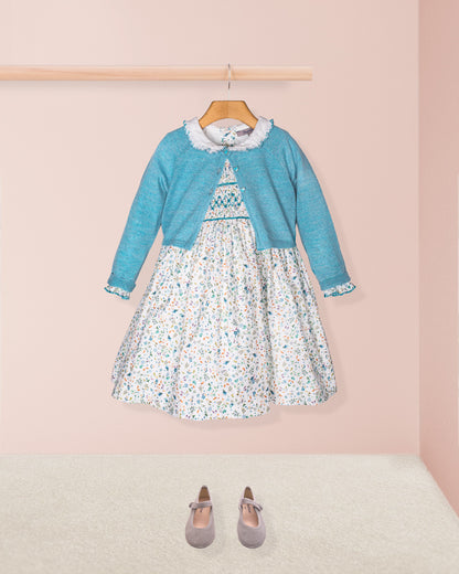 Children's outfit with floral dress and blue cardigan on a pink background