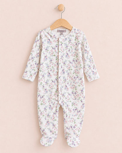 A baby footed sleeper with long sleeves and an all-over small floral print, hanging on a wooden hanger against a solid pale pink background.