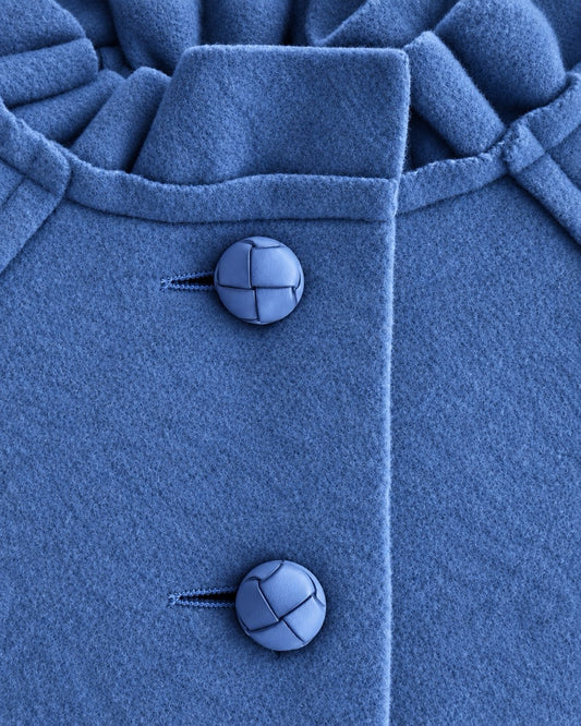 Closeup of blue coat showing 2 top vertical buttons and ruffled neckline