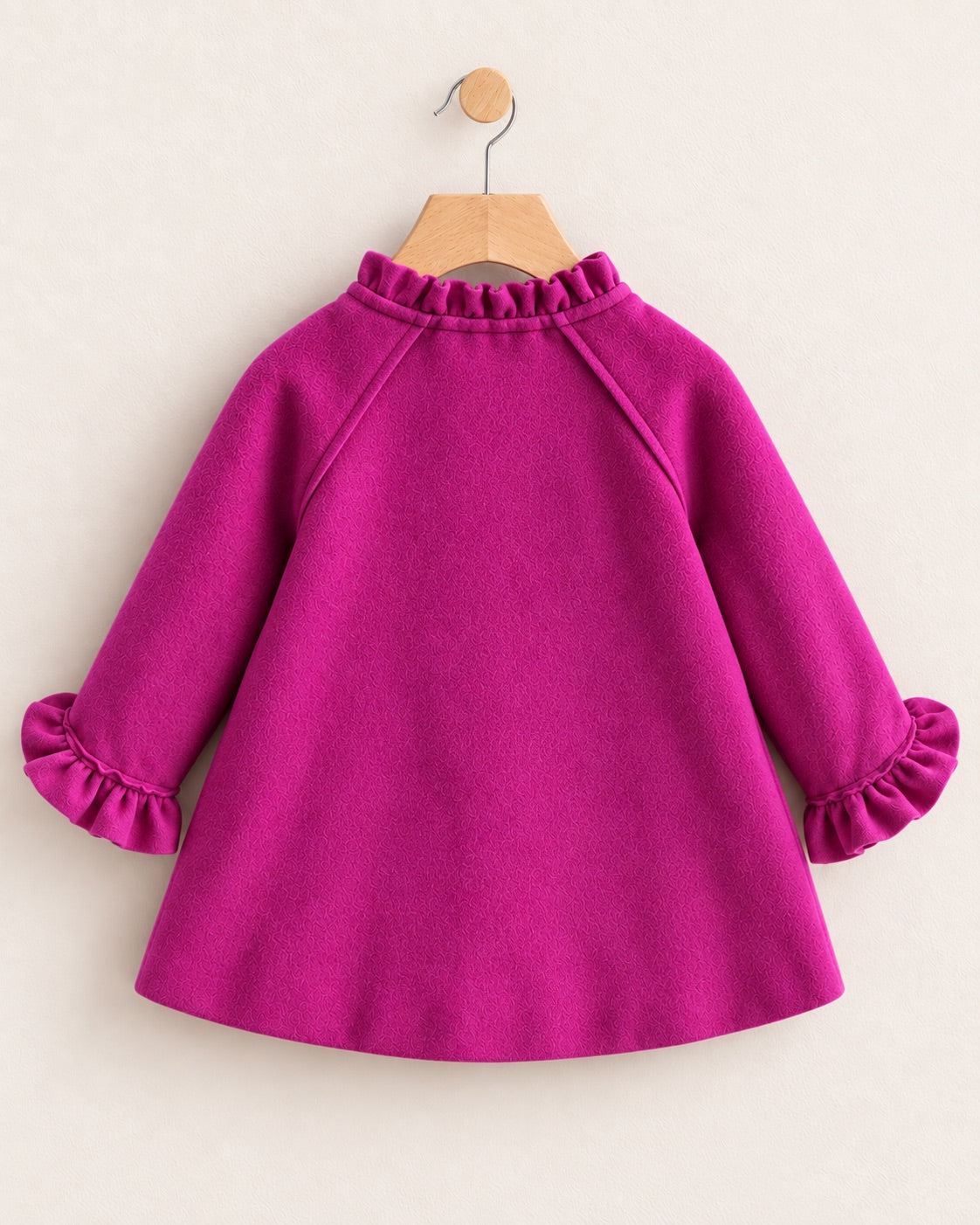 Back of a Redish purple coat on a hanger against a muted pink background