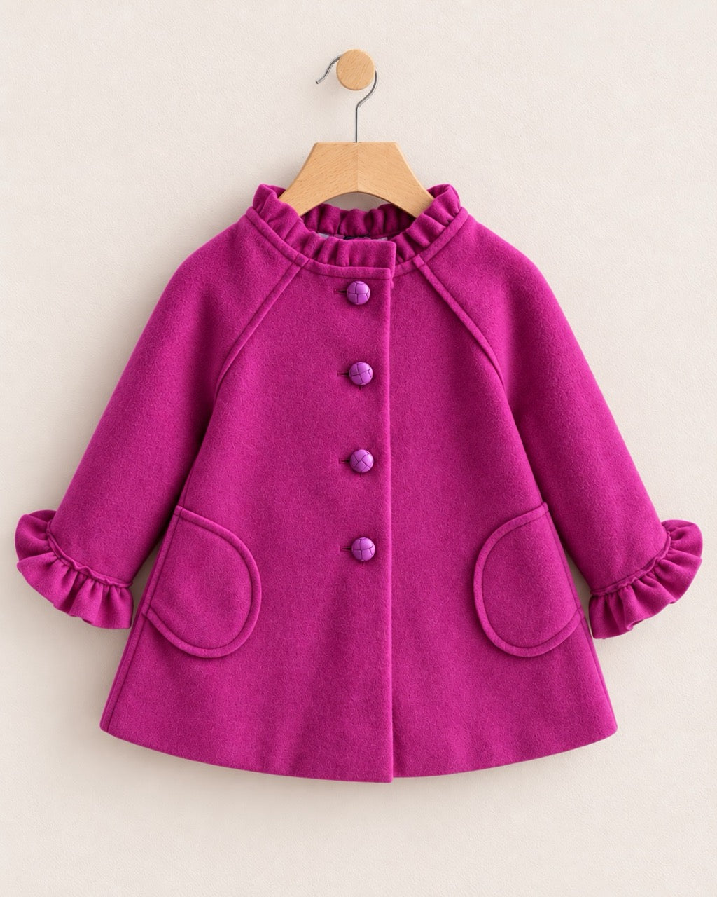 Redish purple coat with 4 buttons and 2 oval shaped pockets, on a hanger against a muted pink background