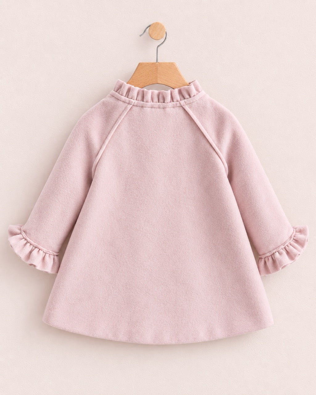 Back of a light pink colored coat, with ruffled neckline, on a hanger against a muted pink background
