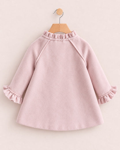 Back of a light pink colored coat, with ruffled neckline, on a hanger against a muted pink background