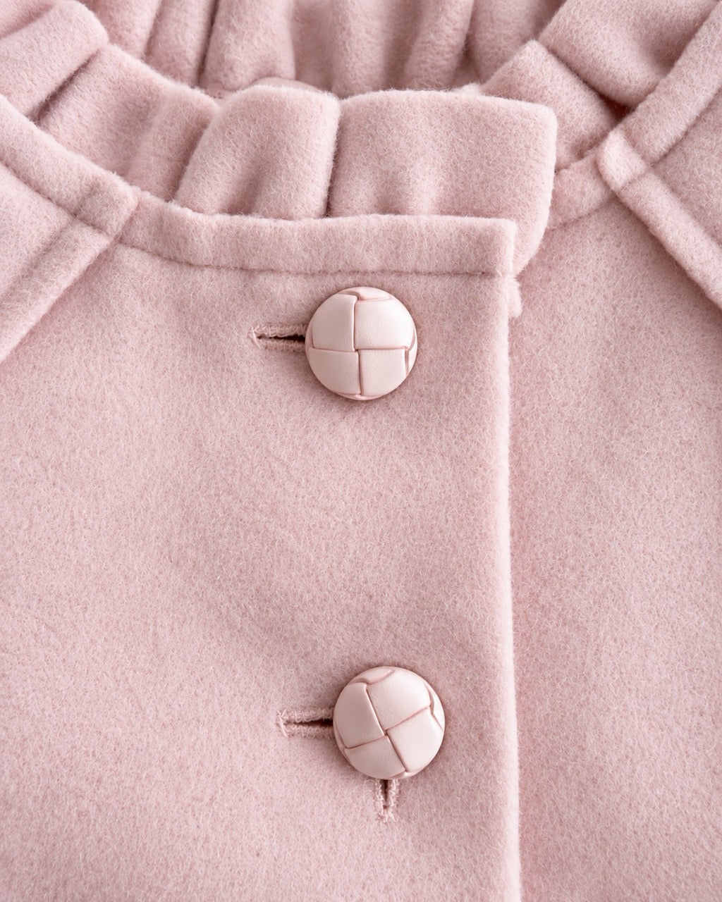 Close up of a light pink colored coat showing 2 top buttons and neckline