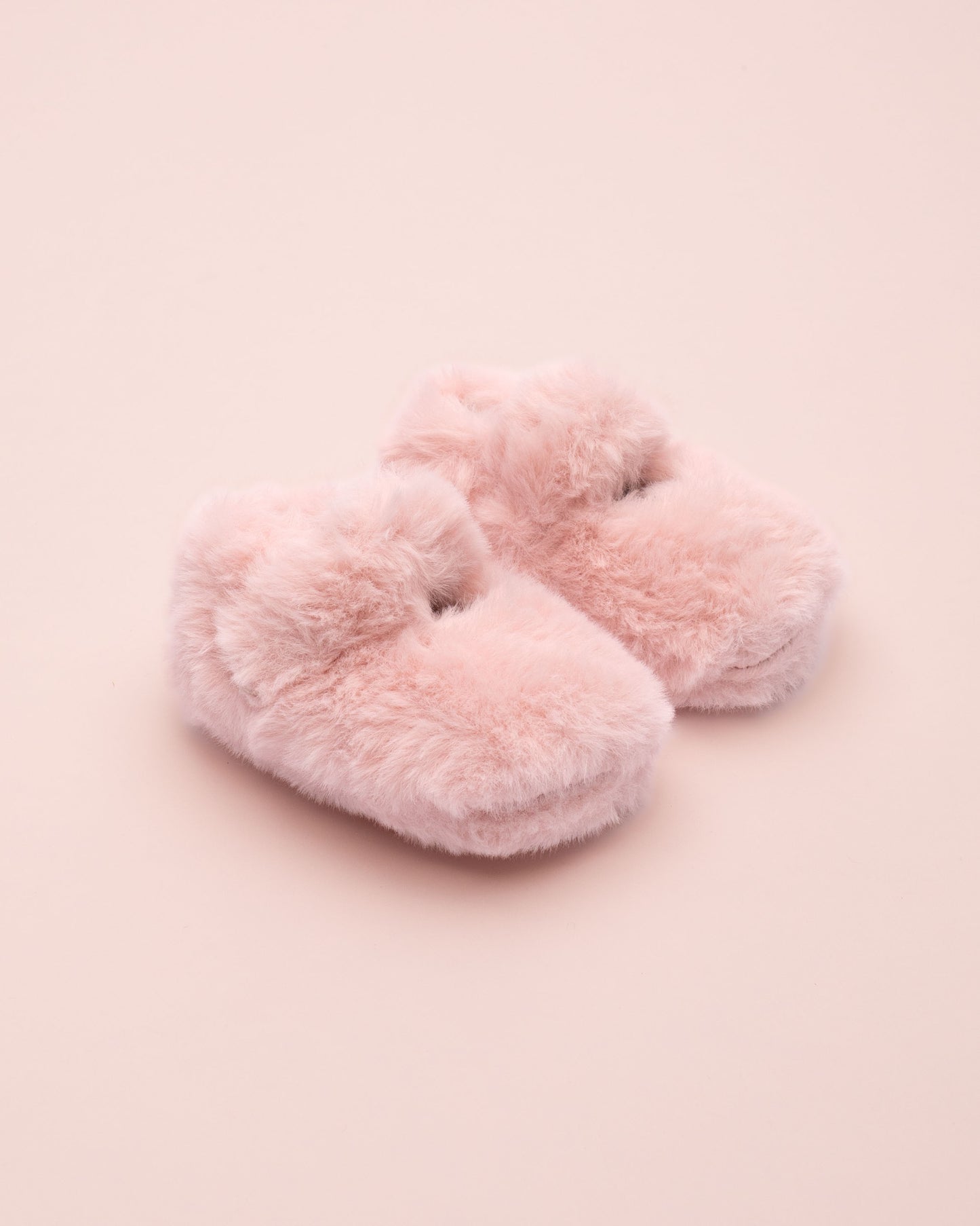 Pair of pink fluffy crib shoe on a pink background