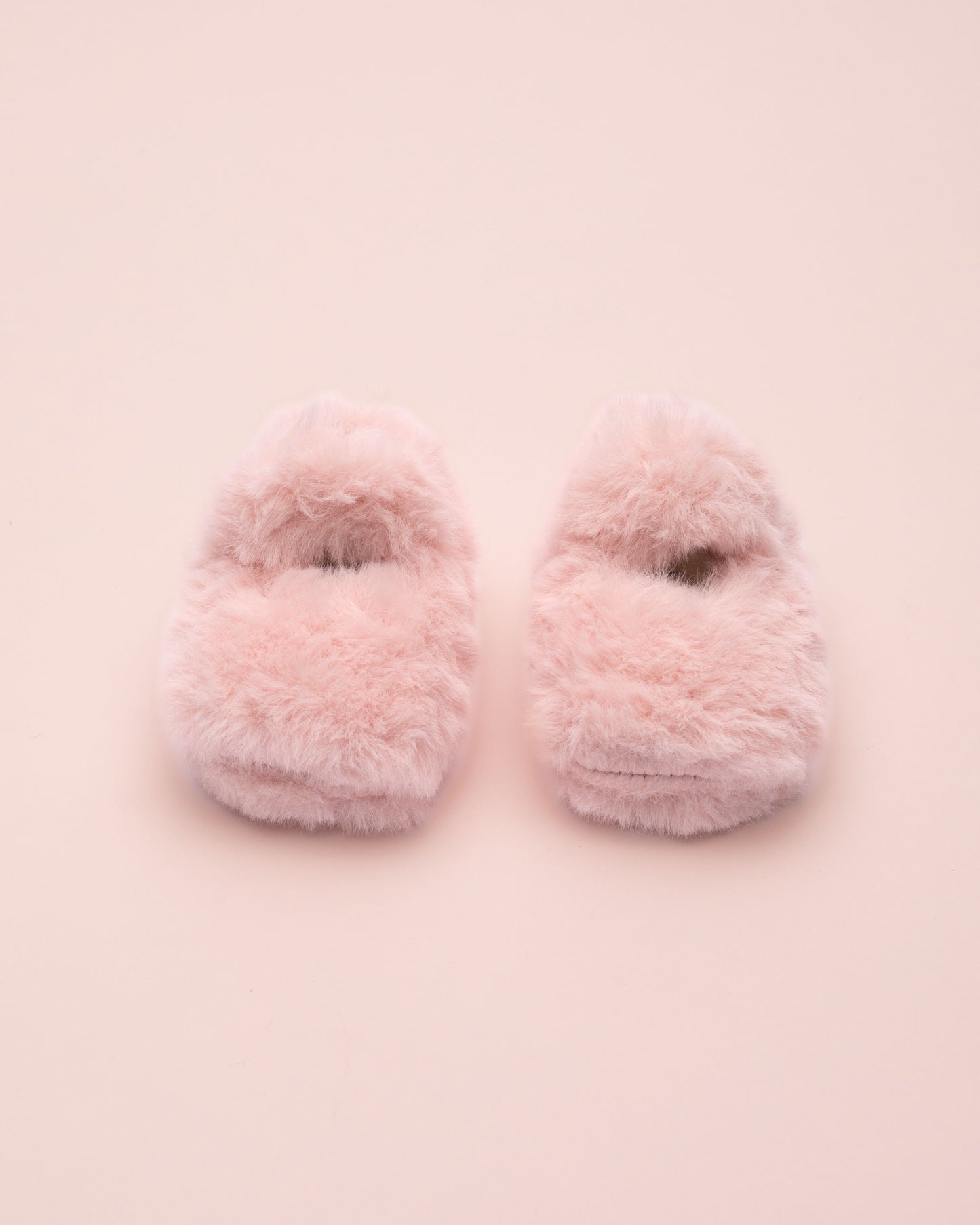 Pair of pink fuzzy crib shoe on a light pink background