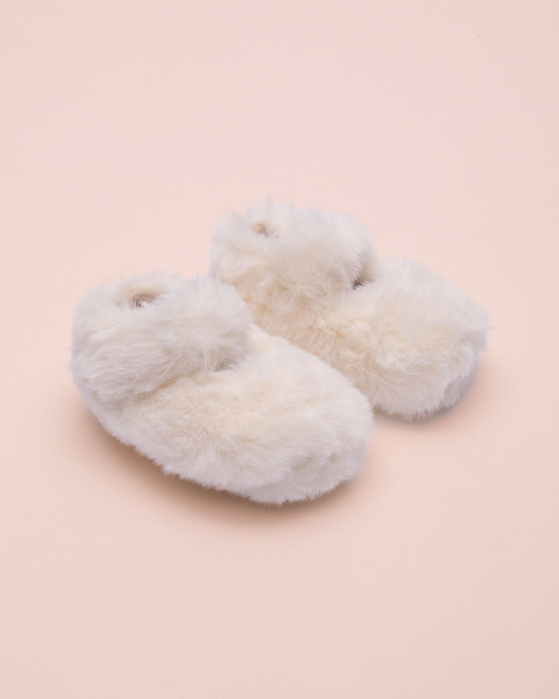 Pair of fluffy white crib shoe on a light pink background