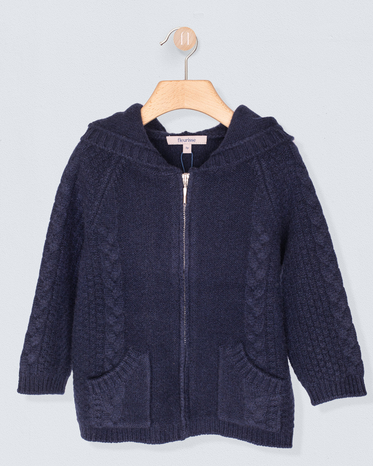 Navy blue knitted hoodie on a wooden hanger against a light gray background