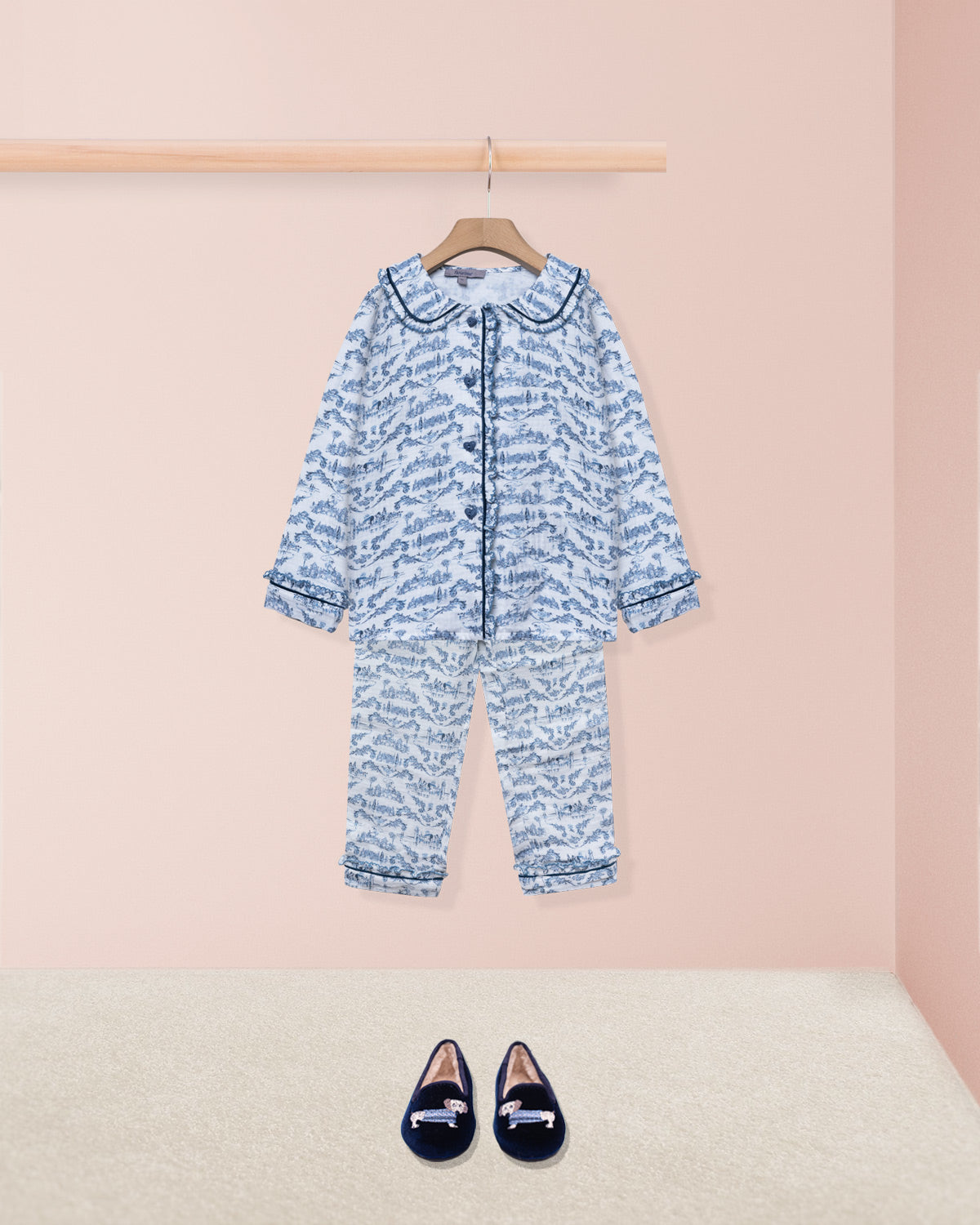 blue girl pajama on hanger with navy house slipper shoe on pink backdrop