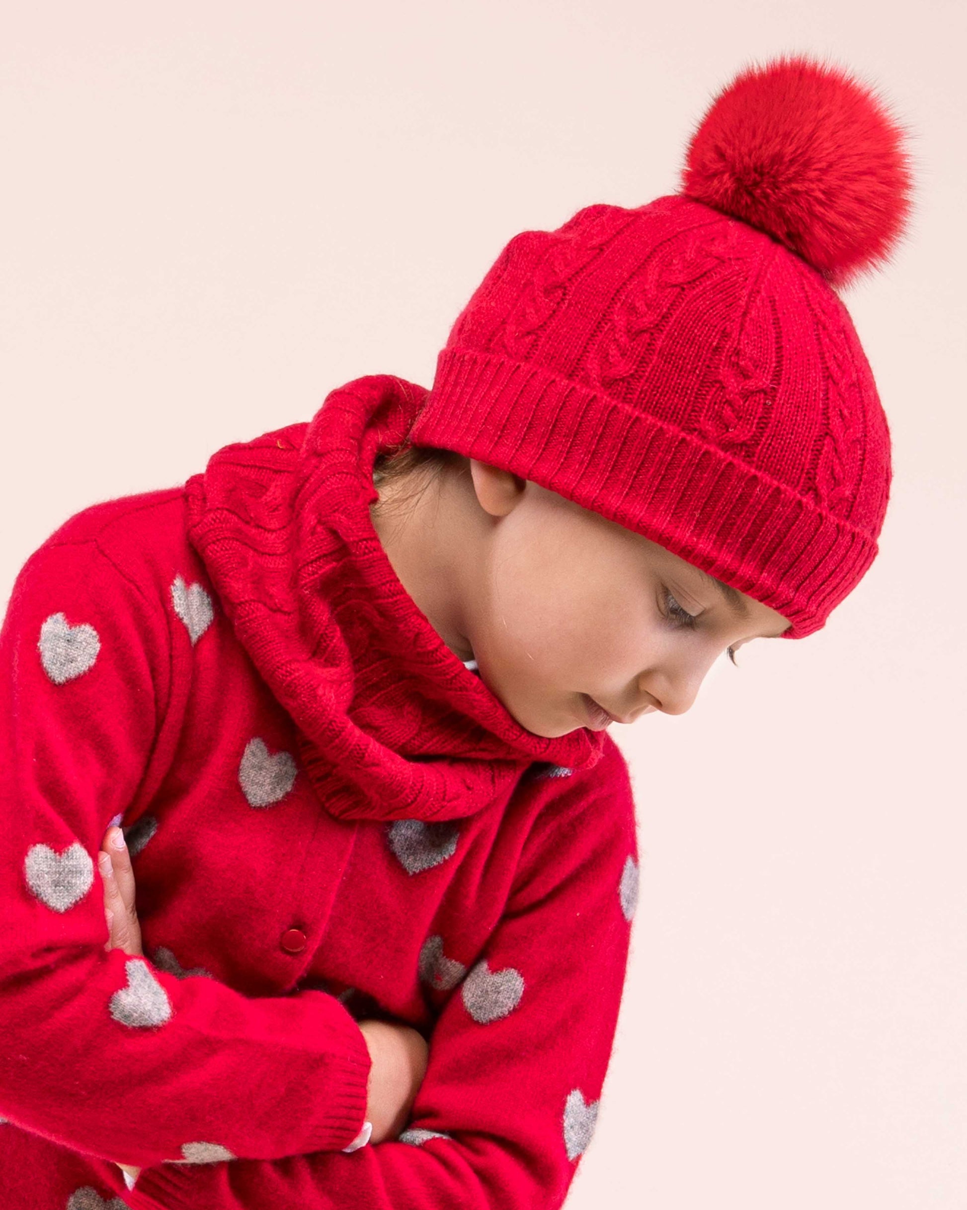 Girl model wearing Cashmere Red Cable Roll Scarf facing to the side wearing a coordinating red cashmere hat and a sweater showing the details of the scarf