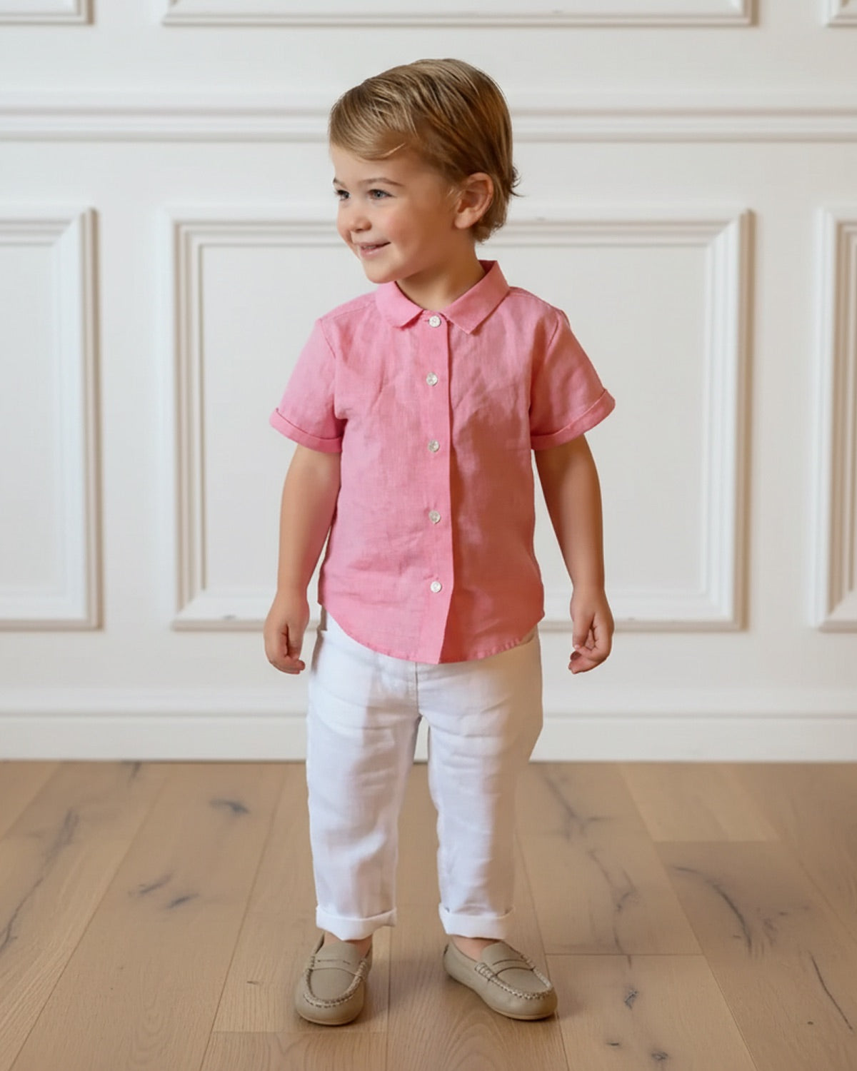 Child wearing a pink shirt and white pants standing in a room with wooden flooring and white paneled walls.
