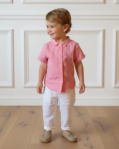 Child wearing a pink shirt and white pants standing in a room with wooden flooring and white paneled walls.