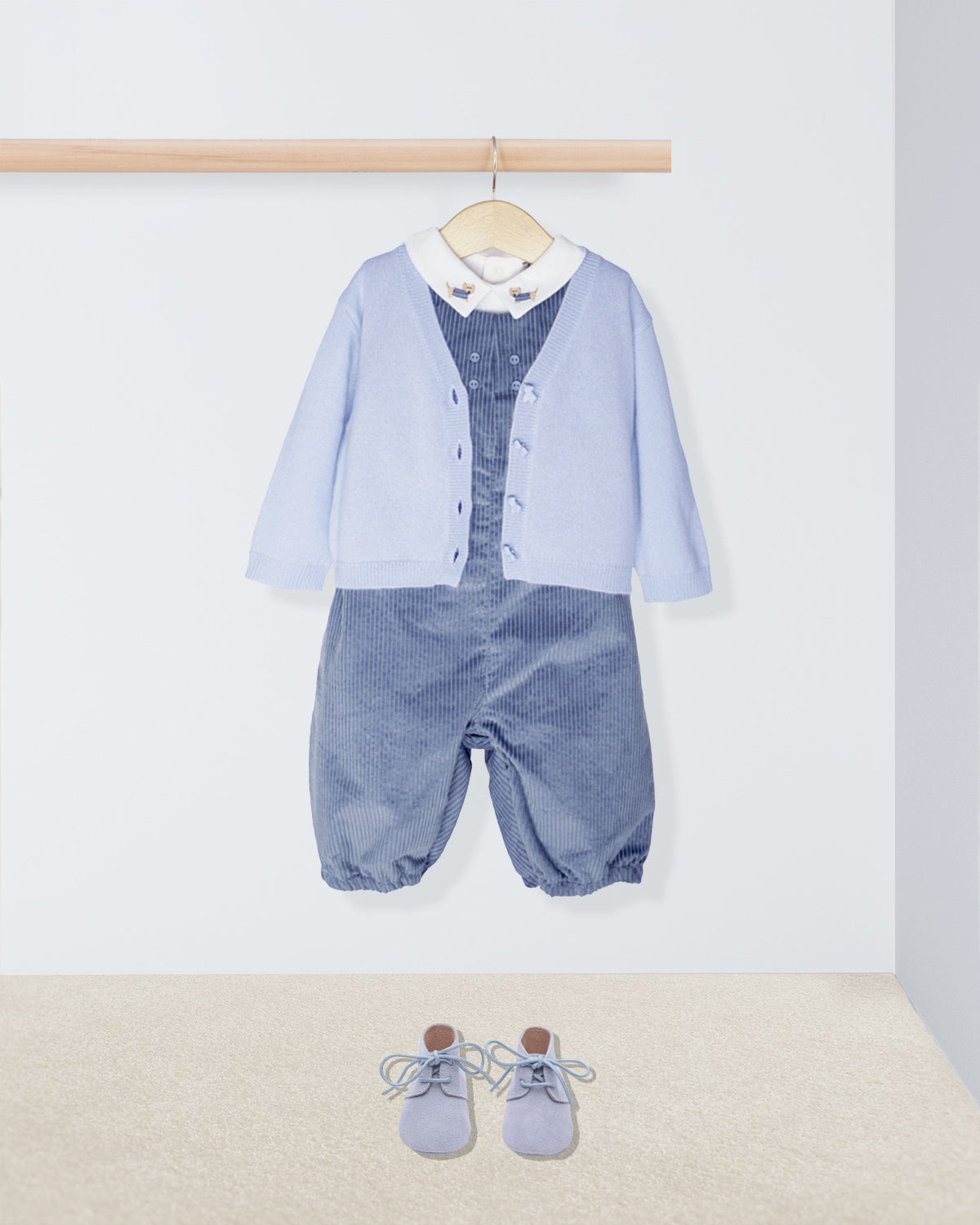 Baby outfit with blue cardigan, shirt, and pants on a hanger against a white background.
