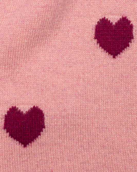 Close up of the fabric of Rose-Pink colored cashmere scarf with red heart patterns on a light pink background