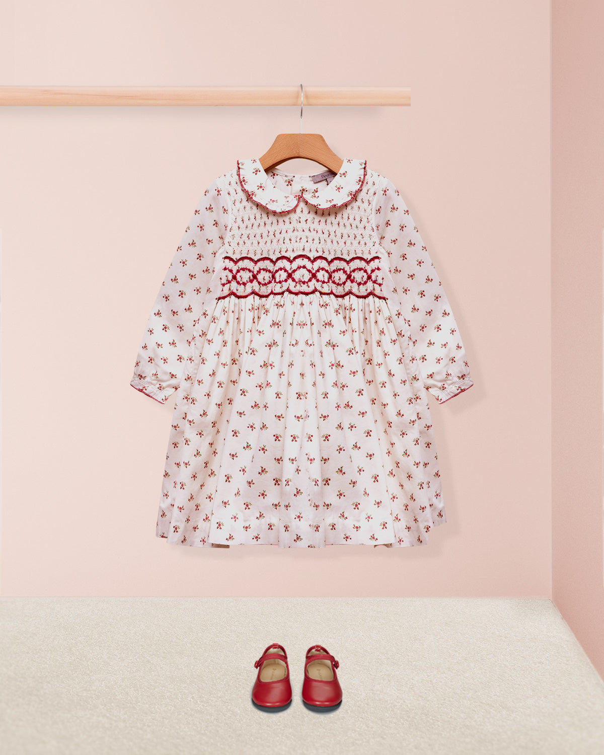 Children's dress with floral pattern and red accents on a pink background