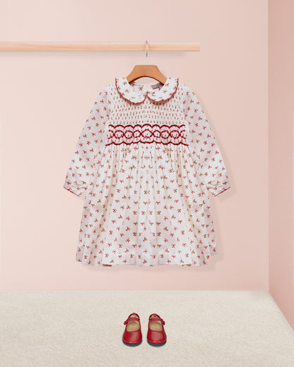 Children's dress with floral pattern and red accents on a pink background