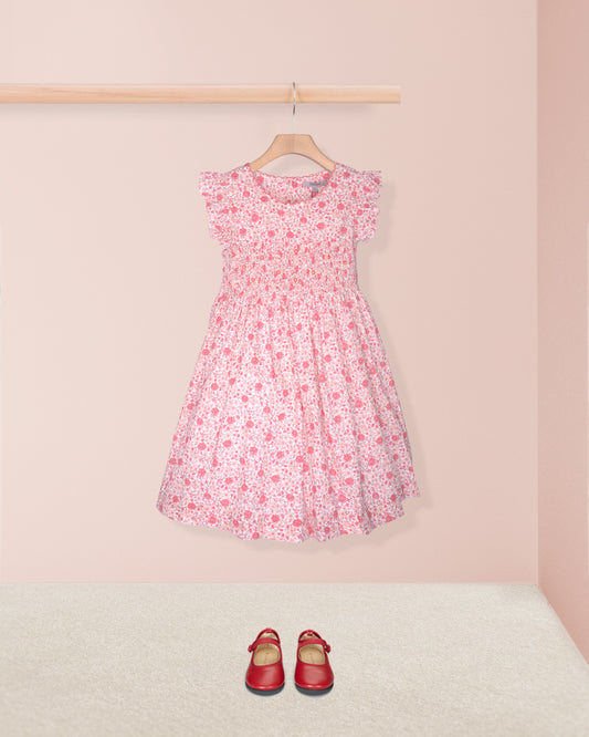 Pink floral dress on a hanger with red shoes on the floor against a pink wall.