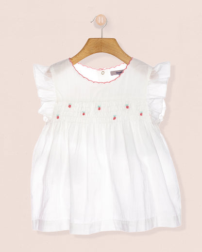 White tunic with strawberry designs on a hanger against a peach background.