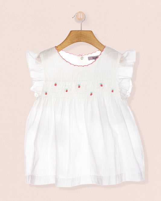 White tunic with strawberry designs on a hanger against a peach background.