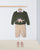 Children's outfit with green sweater featuring a dinosaur design, beige pants, and pink shoes on a white background.