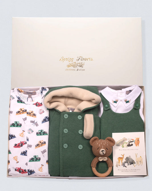Baby clothing set with green vest, patterned blanket, and teddy bear rattle on a light blue background.