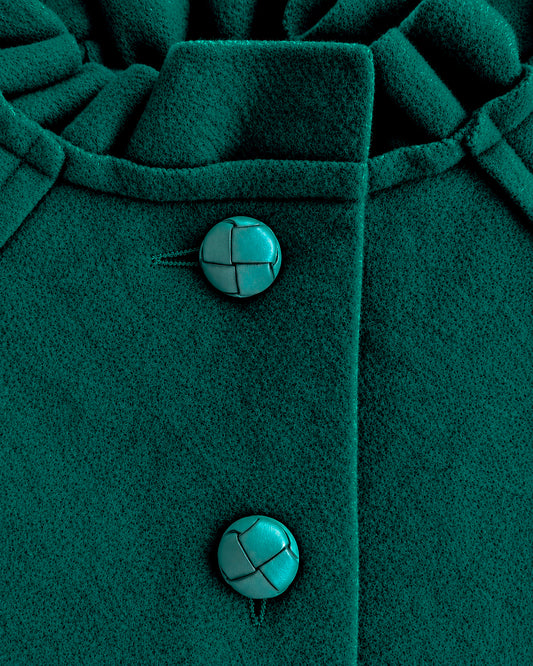 Close-up of a dark hunter-green textured coat with two round turquoise buttons featuring black geometric line details.