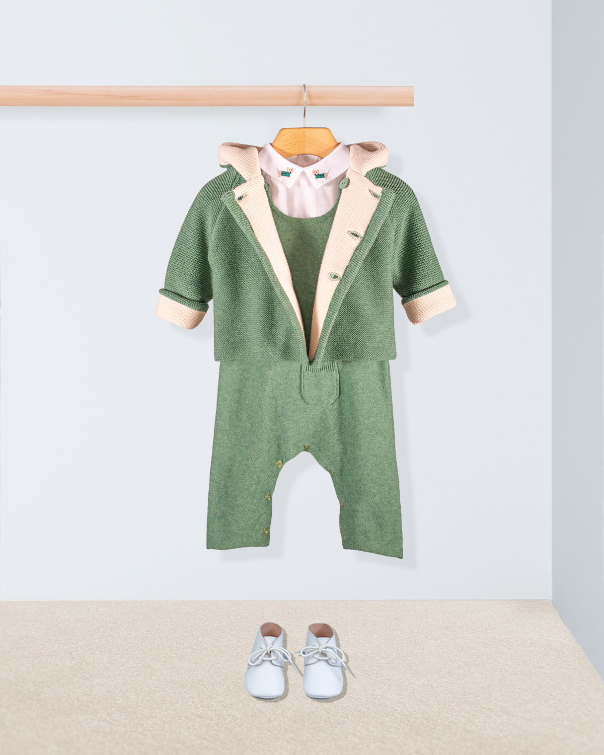 Aspen Sage Melange Cotton Knit Overall layered with a matching green knit jacket and white onesie with embroidered collar paired with white shoes