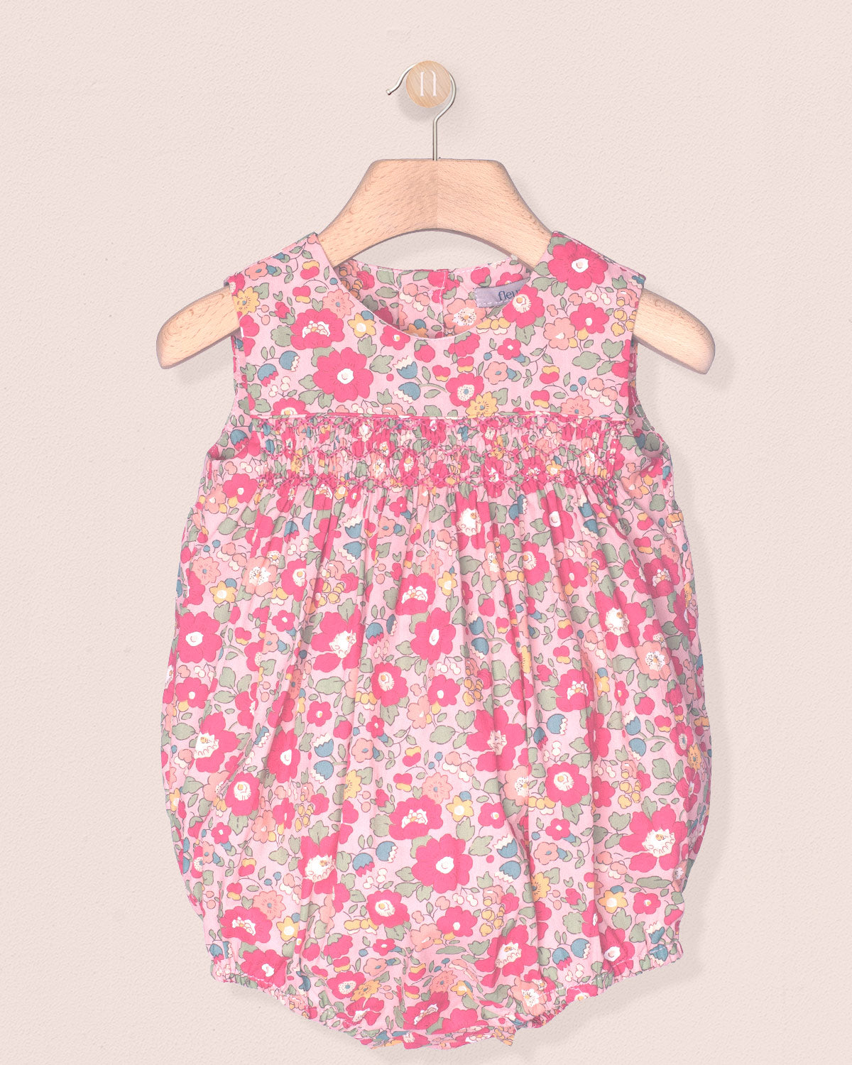 Floral-patterned baby dress on a hanger against a beige background