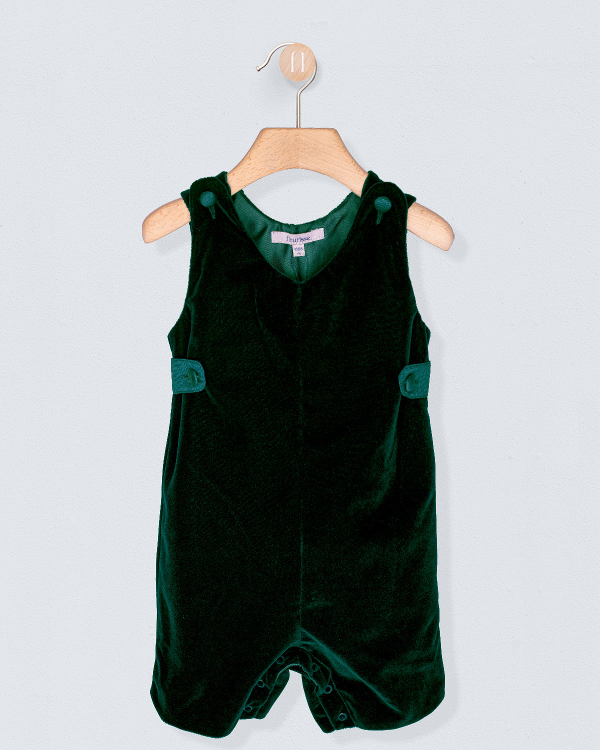 Green velvet romper with straps on a wooden hanger against a light gray background